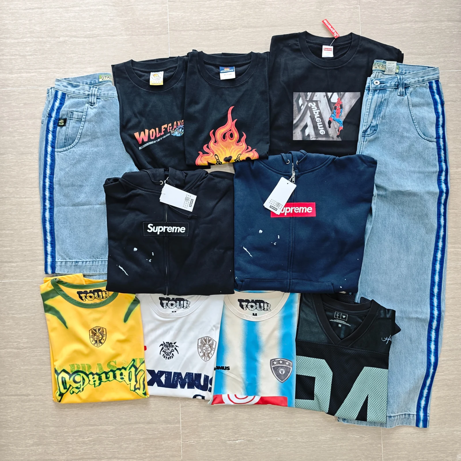 Flat-lay overview of black graphic T-shirts, blue-striped denim, two paint-splatter hoodies and football-style tops.