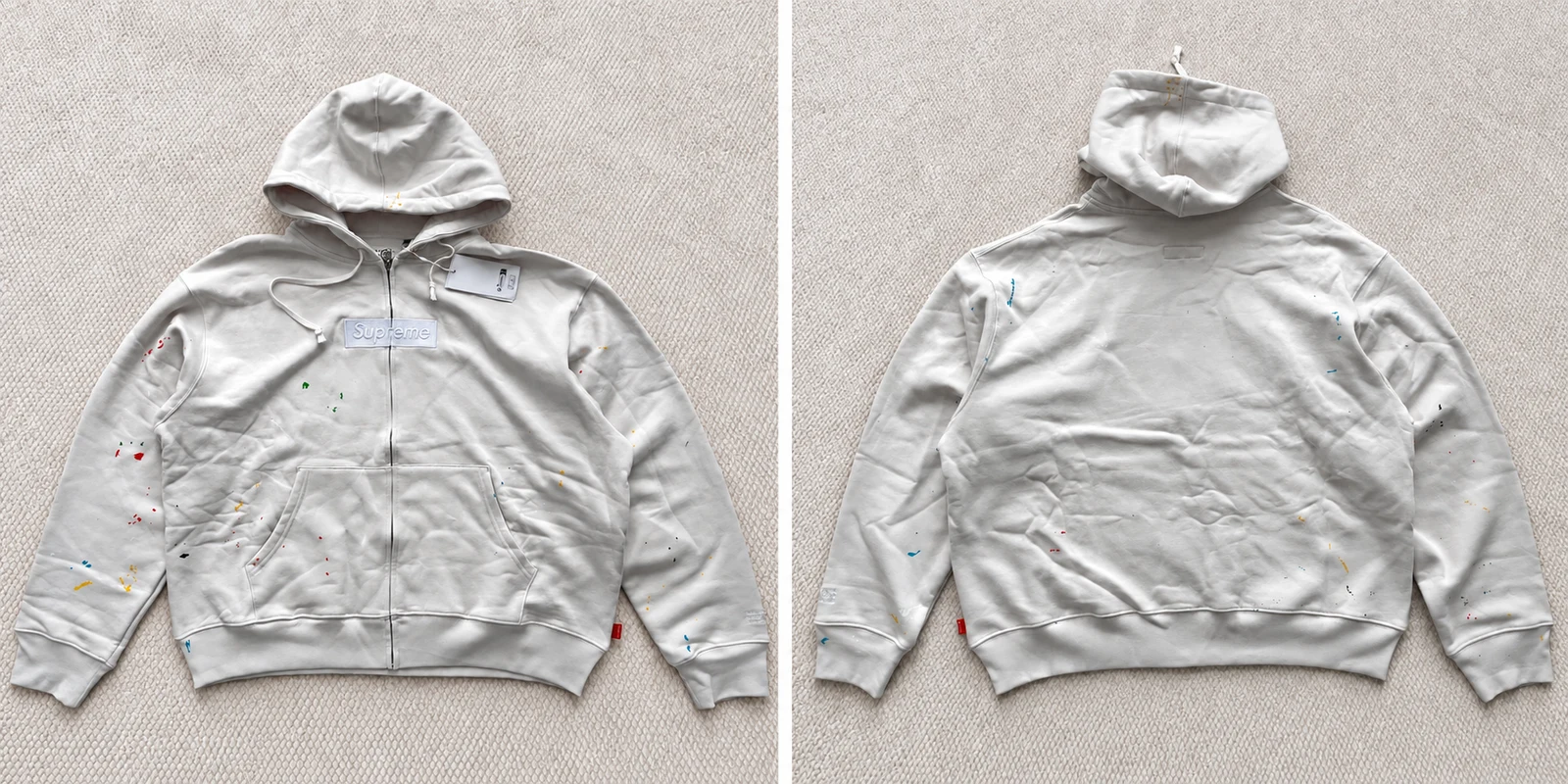 Two-panel front and back views of a light-grey hoodie with scattered paint-style marks.