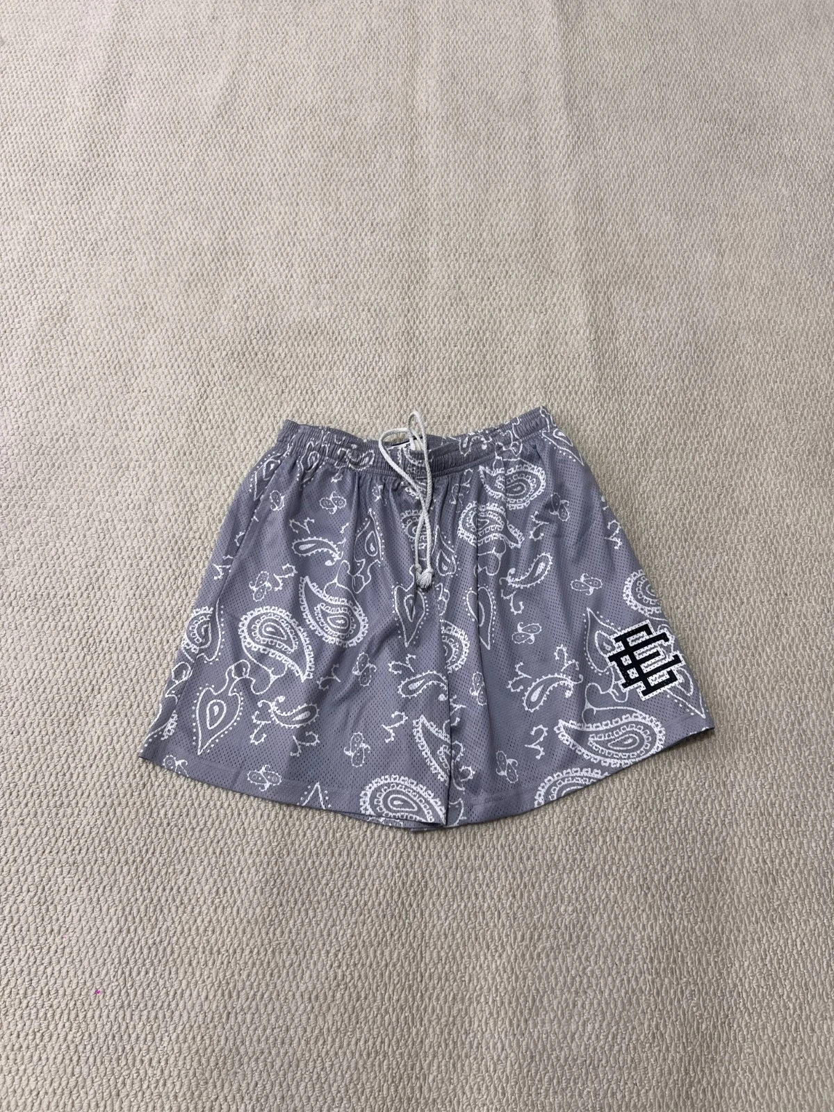 Grey shorts with an all-over paisley pattern and contrasting lower-leg logo patch.