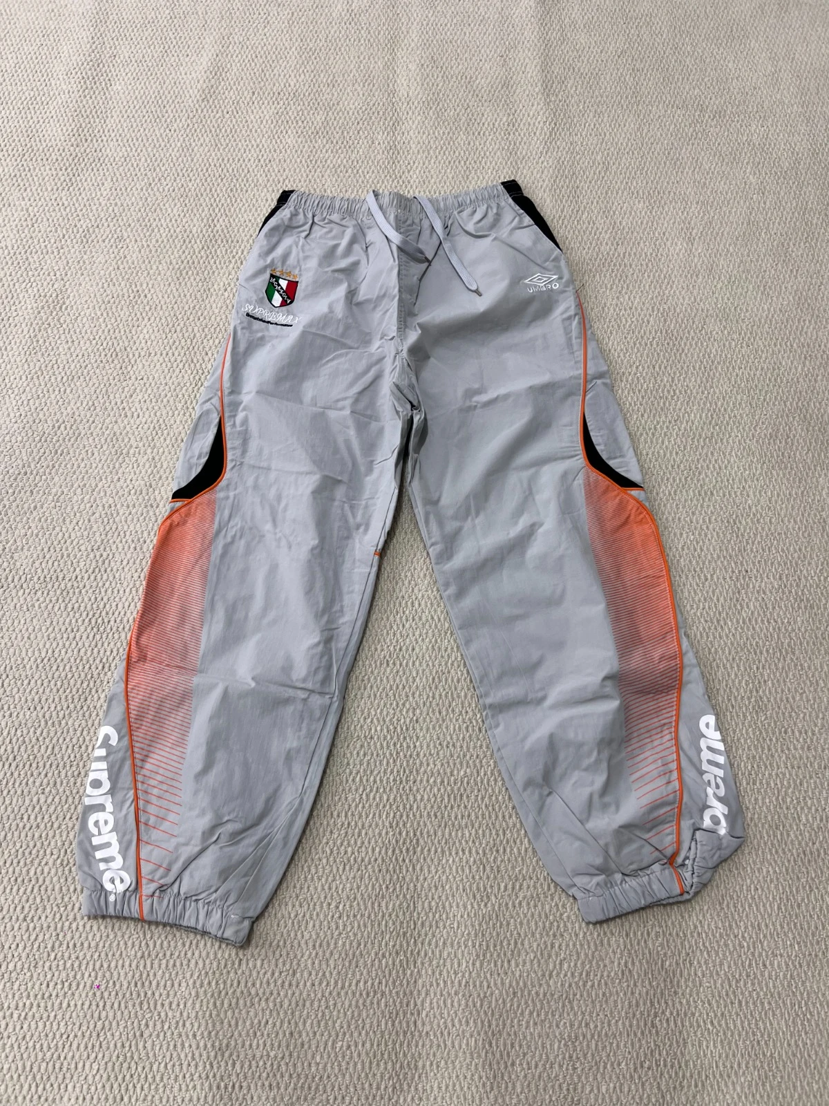 Grey trousers with orange side panels and white lettering near the lower legs.